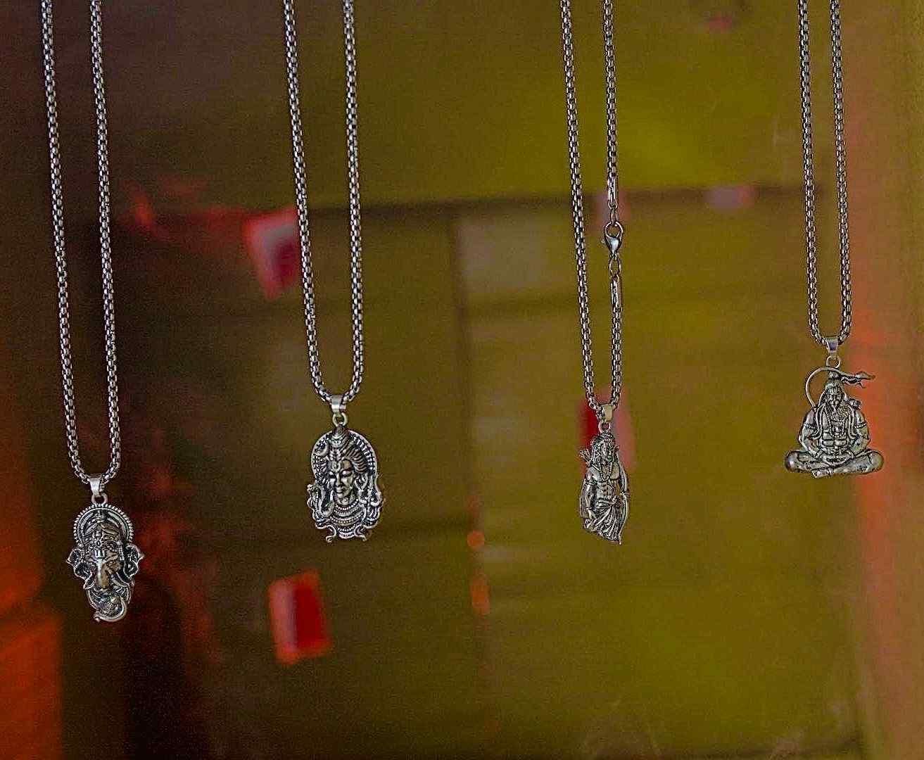 Four silver necklaces with various pendants on a reflective surface.